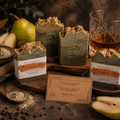 Three bars of ESPUMA Apothecary Bourbon Pear Olive Oil Handmade Soap with kaolin clay and blue agave, displayed on a rustic wooden board with fresh pears, a crystal whiskey glass, kaolin clay powder, and a bilingual affirmation card on a dark moody surface.