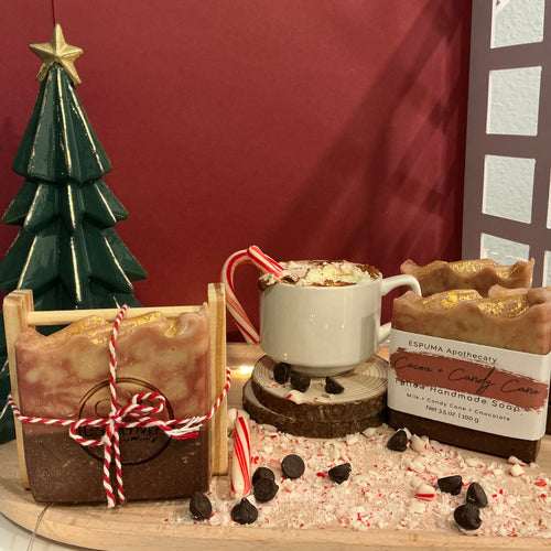 Handmade Cocoa and Candy Cane soap by Espuma Apothecary displayed with a hot chocolate mug, candy canes, and a small Christmas tree on a wooden surface.