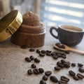 Open glass jar of Espresso Coffee Latte sugar scrub with a whipped brown texture, surrounded by coffee beans and a ceramic cup on a neutral surface.