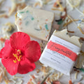 Fragmentos handmade soap by Espuma Apothecary displayed in light bars with colorful soap pieces and a red hibiscus flower on a neutral surface.