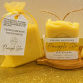Pineapple Glow handmade soap by Espuma Apothecary displayed with a yellow organza gift bag on a gold glitter background.