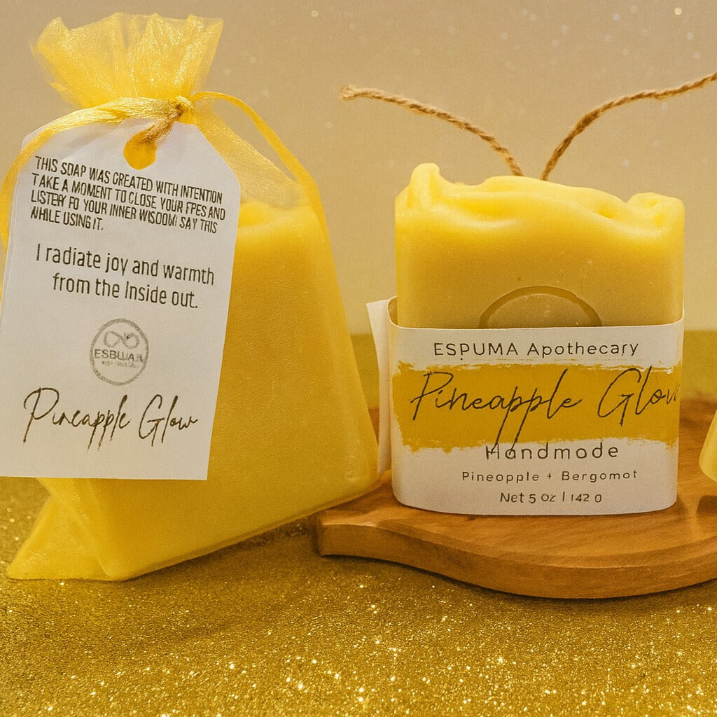 Pineapple Glow handmade soap by Espuma Apothecary displayed with a yellow organza gift bag on a gold glitter background.